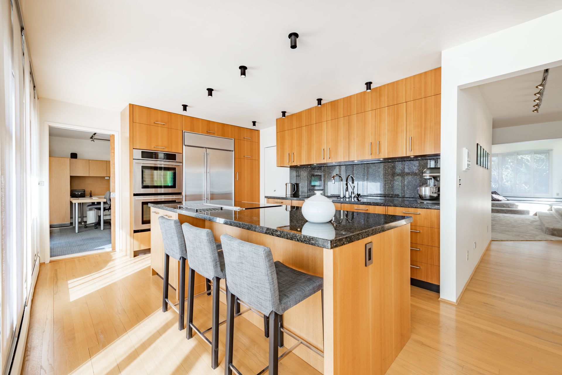 Modern kitchen with light wood cabinets, dark granite countertops, and a central island with bar stools.