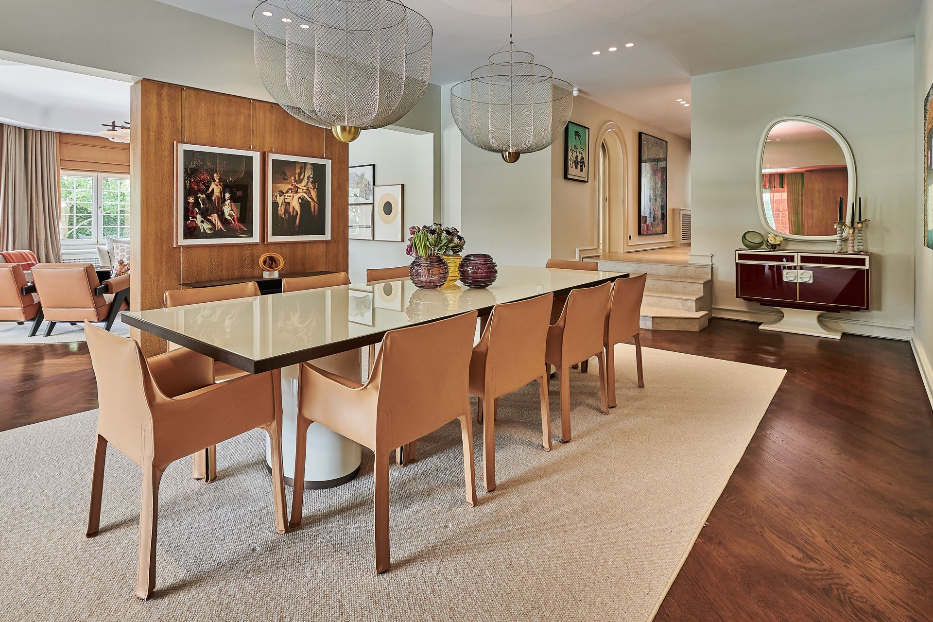 Elegant dining room with a long table, tan chairs, and decorative light fixtures.