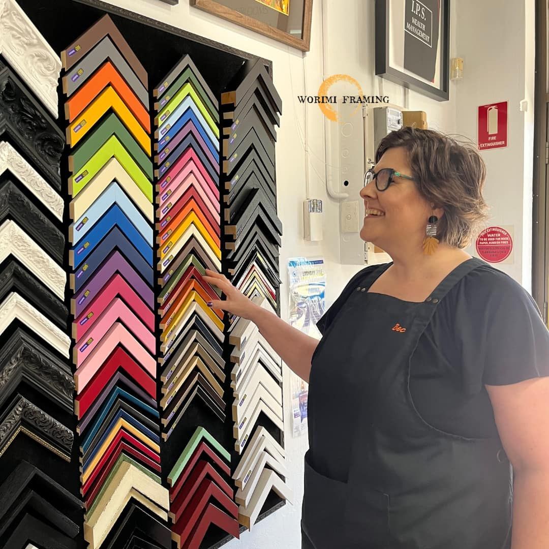 A Woman Is Standing In Front Of A Display Of Picture Frames — Worimi Framing Service In Newcastle, NSW