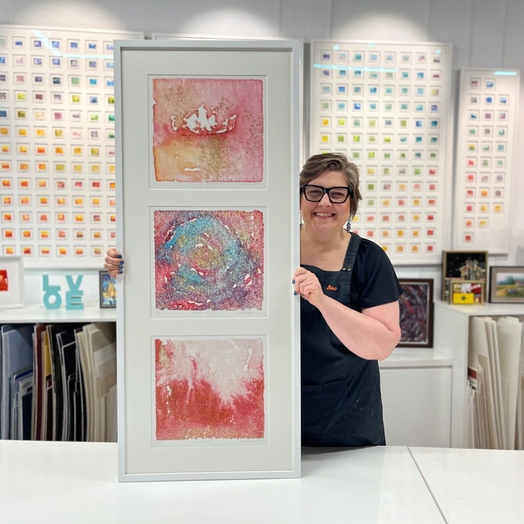 A Woman Is Holding A Framed Painting In A Studio — Worimi Framing Service In Adamstown, NSW