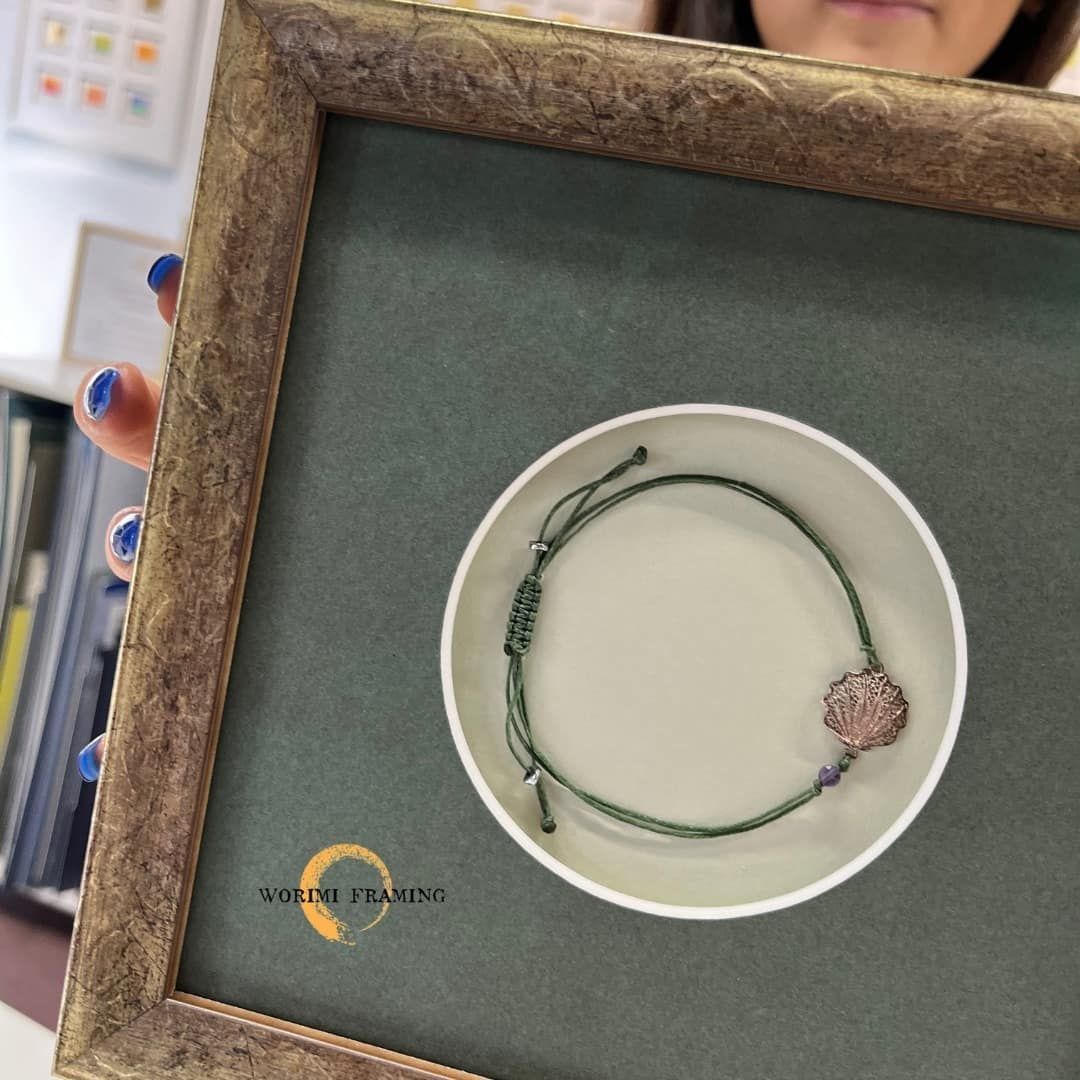 A Woman Is Holding A Picture Frame With A Bracelet In It — Worimi Framing Service In Central Coast, NSW