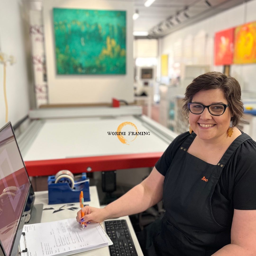 A Woman Is Sitting At A Desk With A Computer And A Pen And Paper — Worimi Framing Service In Maitland, NSW