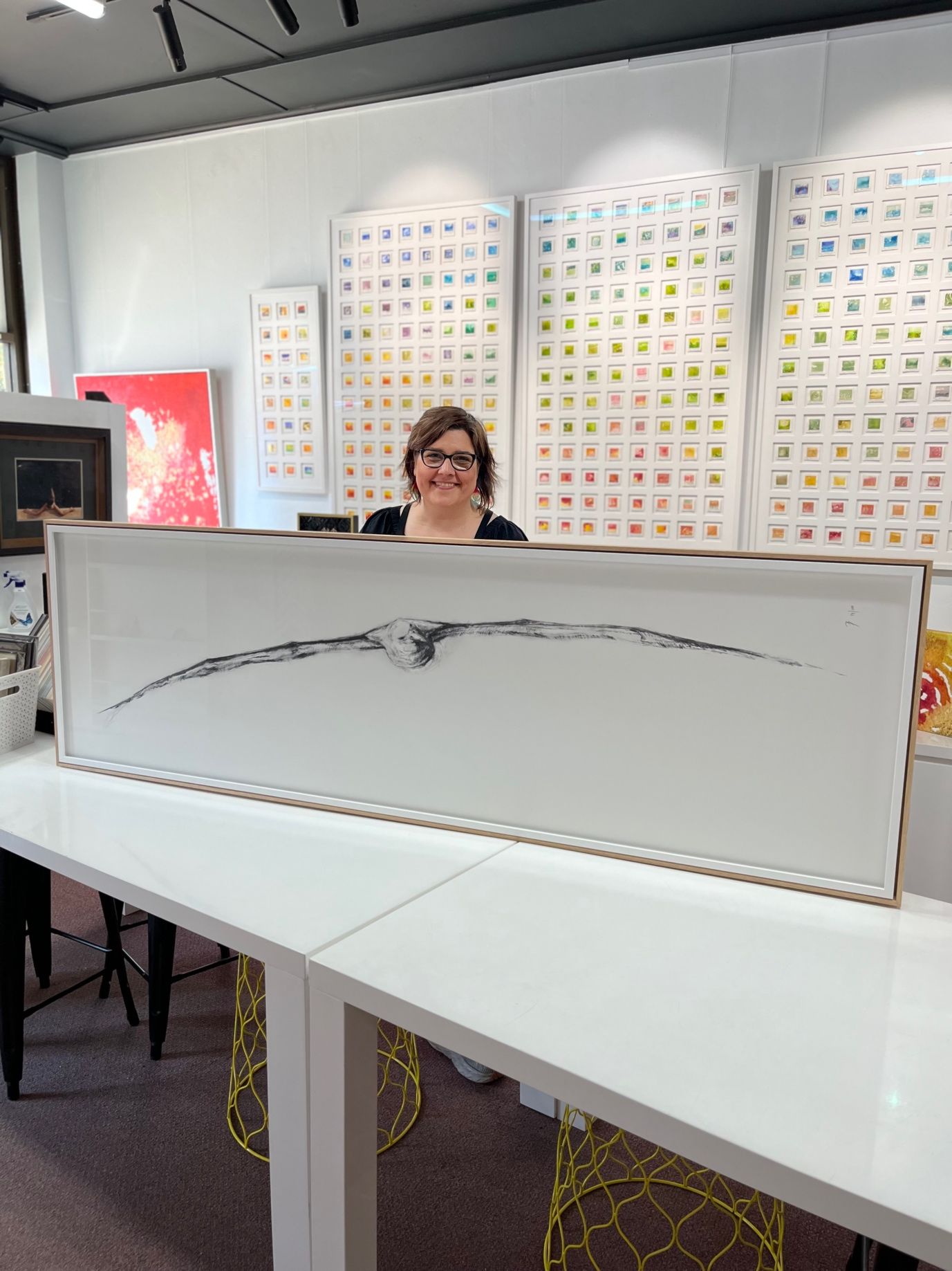 A Woman Is Holding A Framed Photo Infront Of A Wall Of Paintings — Worimi Framing Service In Adamstown, NSW