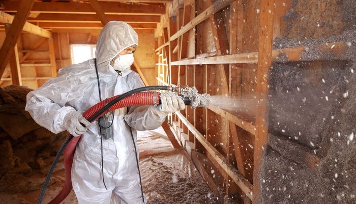 A man wearing a gas mask is spraying foam on a wall.