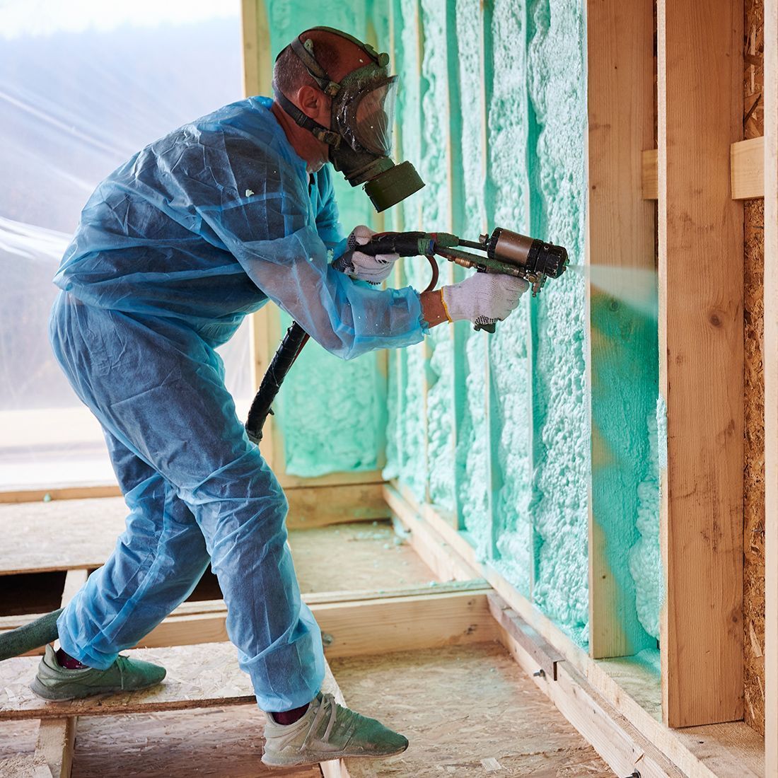 A man wearing a gas mask is spraying foam on a wall.