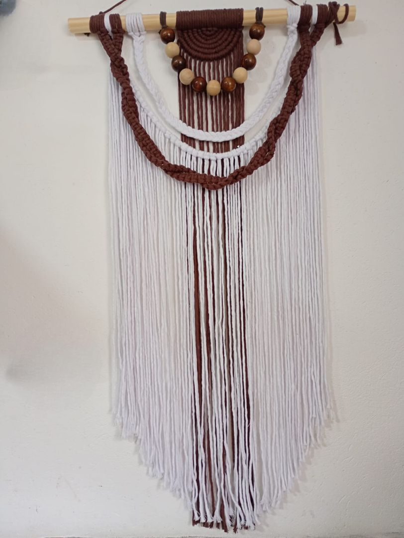 Tapiz de macramé con hilo marrón y blanco, cuentas de madera y una varilla de madera natural.