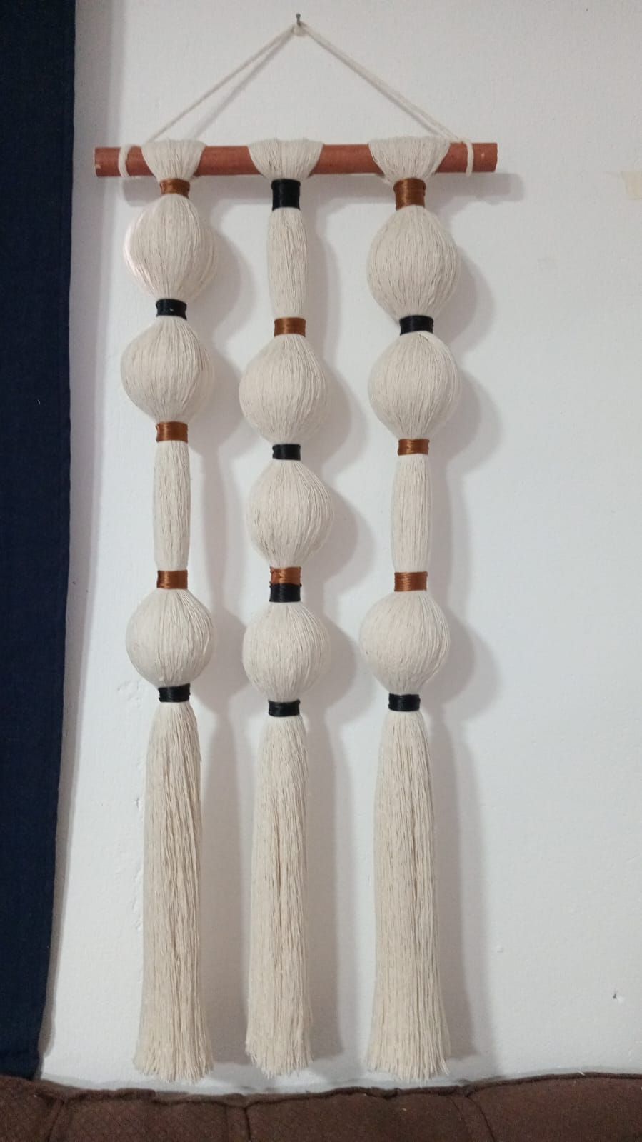Tapiz de pared con bolas de hilo blanco, borlas y detalles de madera.