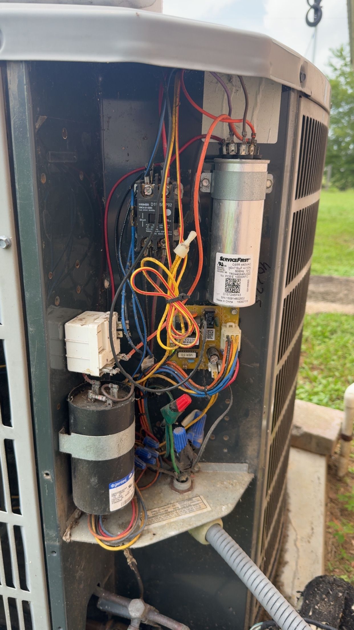 Open panel of an air conditioning unit with wiring, capacitors, and a motor visible.
