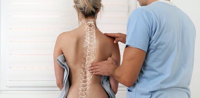 A man is examining a woman 's back with a diagram of the spine on it.