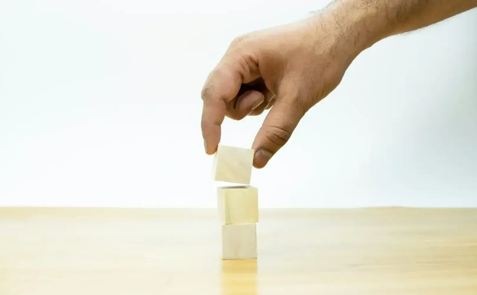 Hand placing a white block on top of stacked white blocks on a table