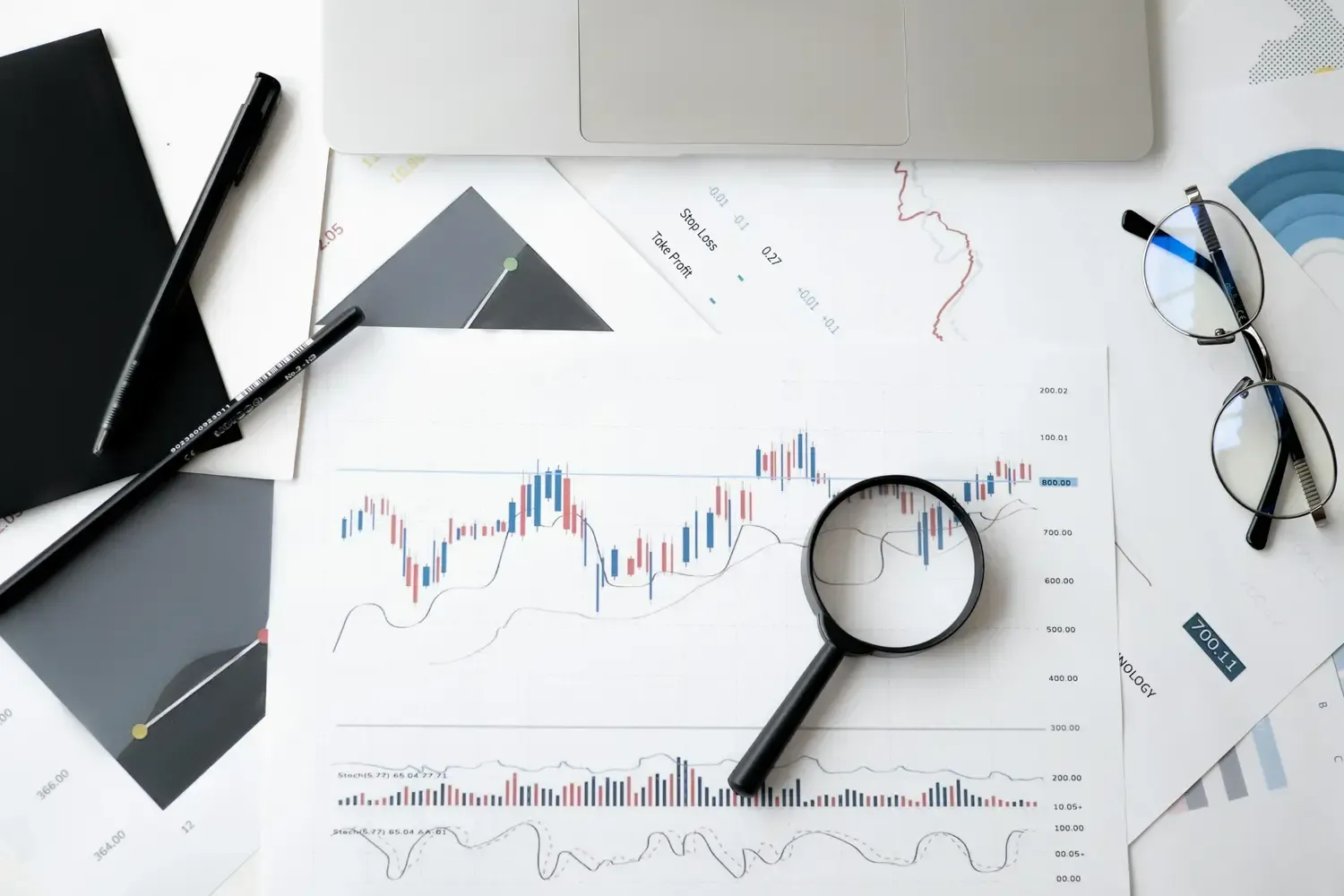 Desk with stock charts, magnifying glass, glasses, and notebook, suggesting financial analysis