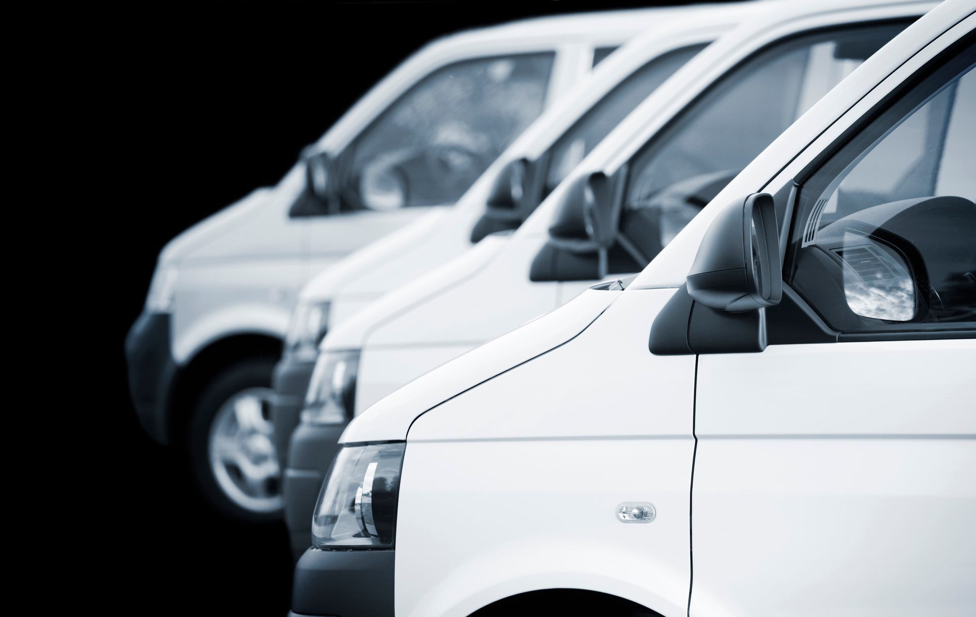 A row of white vans are parked in a row on a black background.