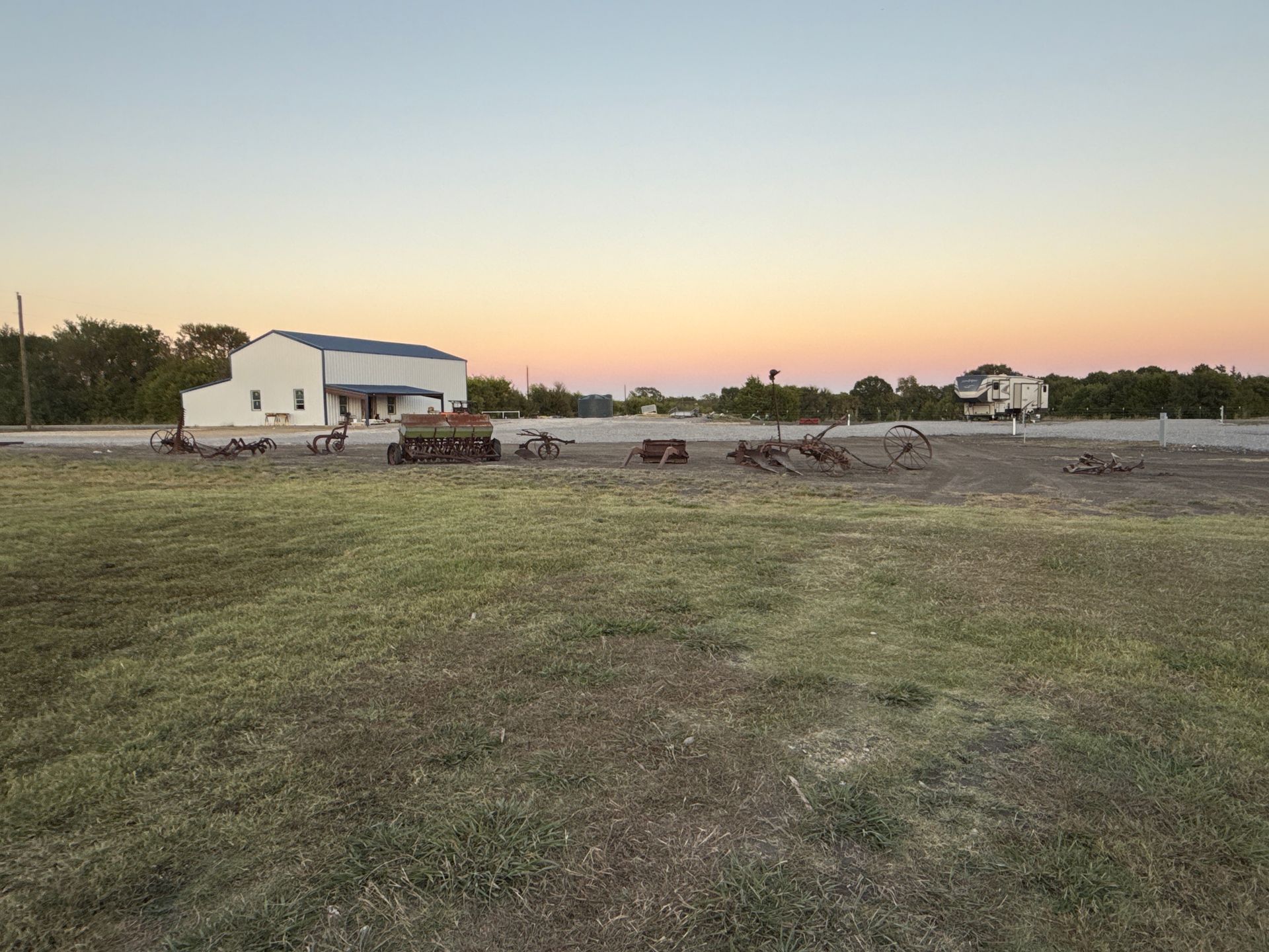Open field with scattered metal objects and a white building at sunset.