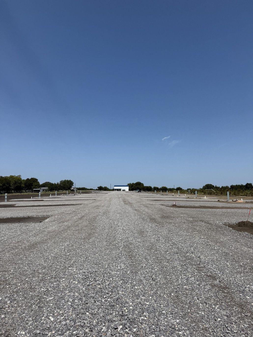 Gravel parking area under a clear blue sky, with a white building in the distance.