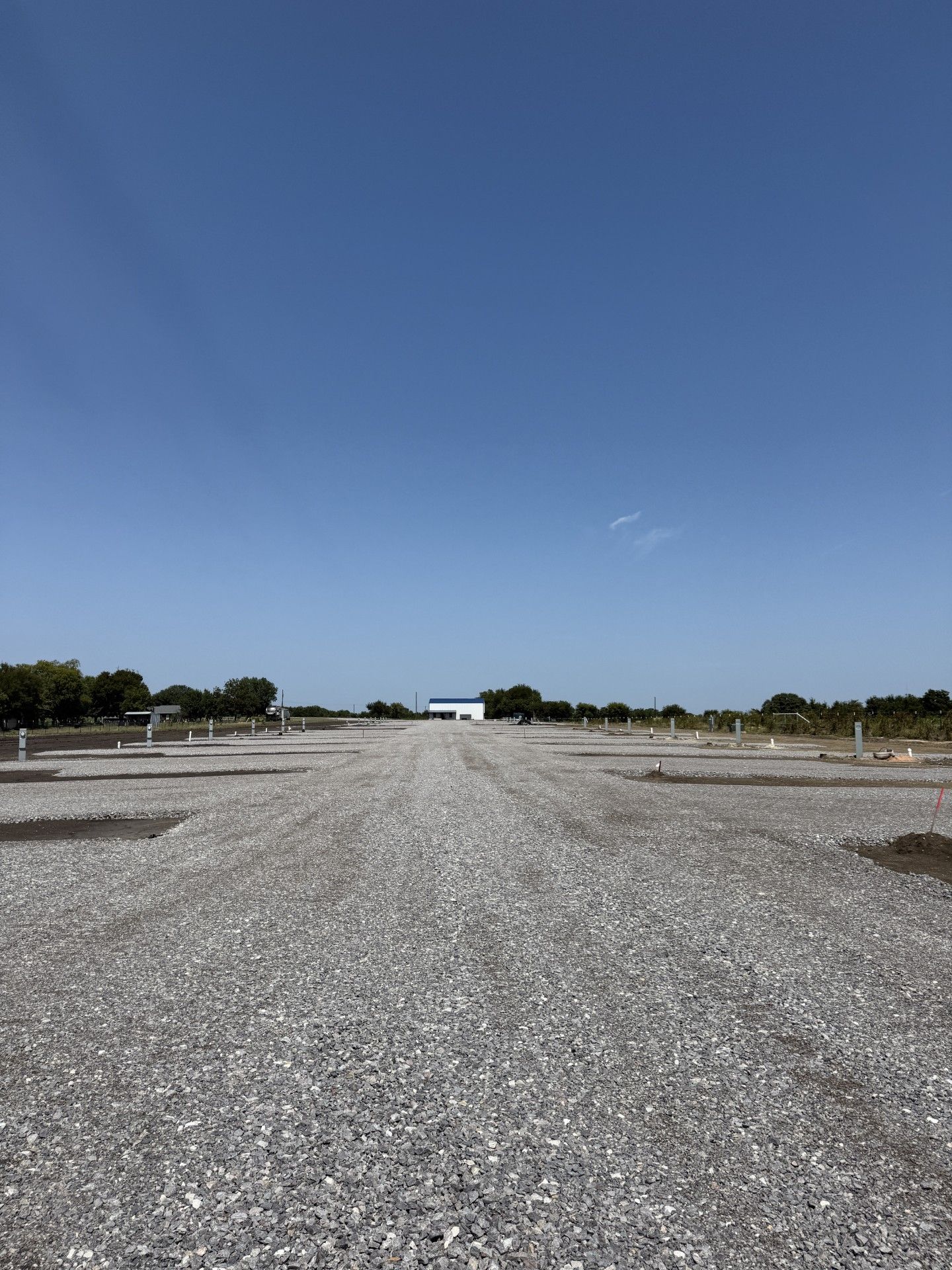 Gravel lot with a white and blue building in the distance, under a clear blue sky.