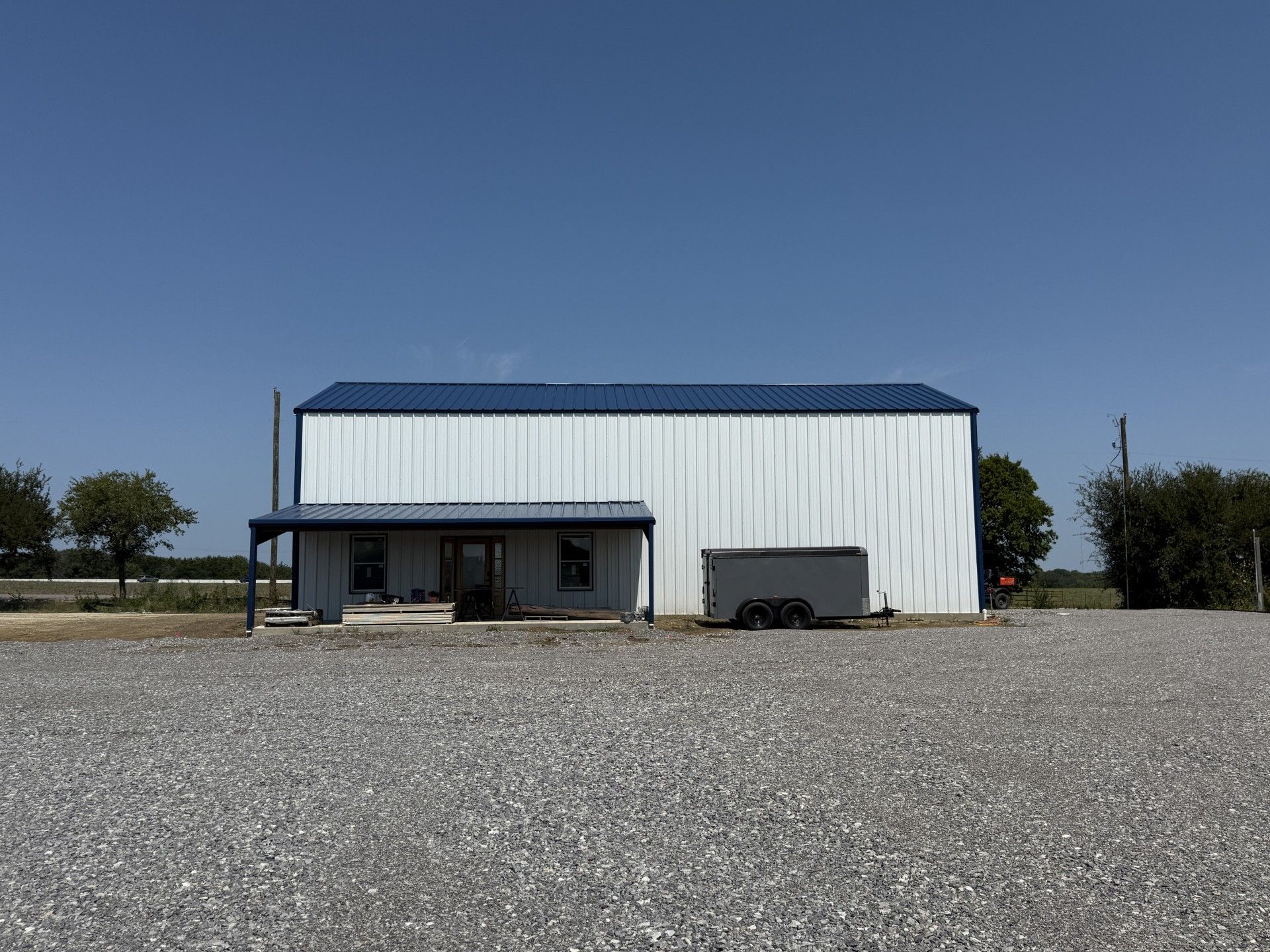 White building with blue roof, small porch, and gravel lot under a clear blue sky.