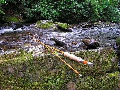 Fly Fishing Rods Balanced on a Mossy Rock with Flowing River in the Background