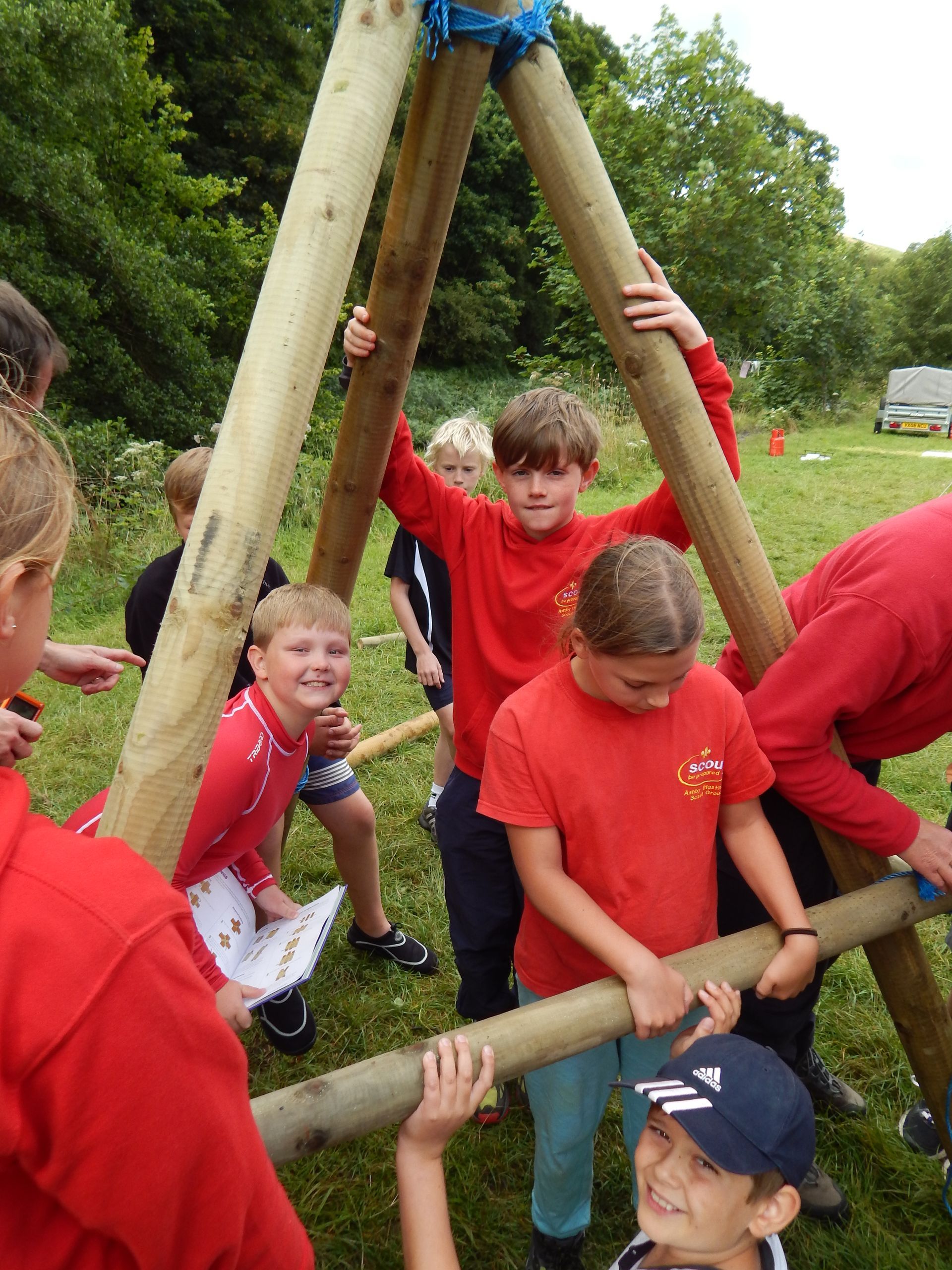 A group of children in red shirts are working on a wooden structure