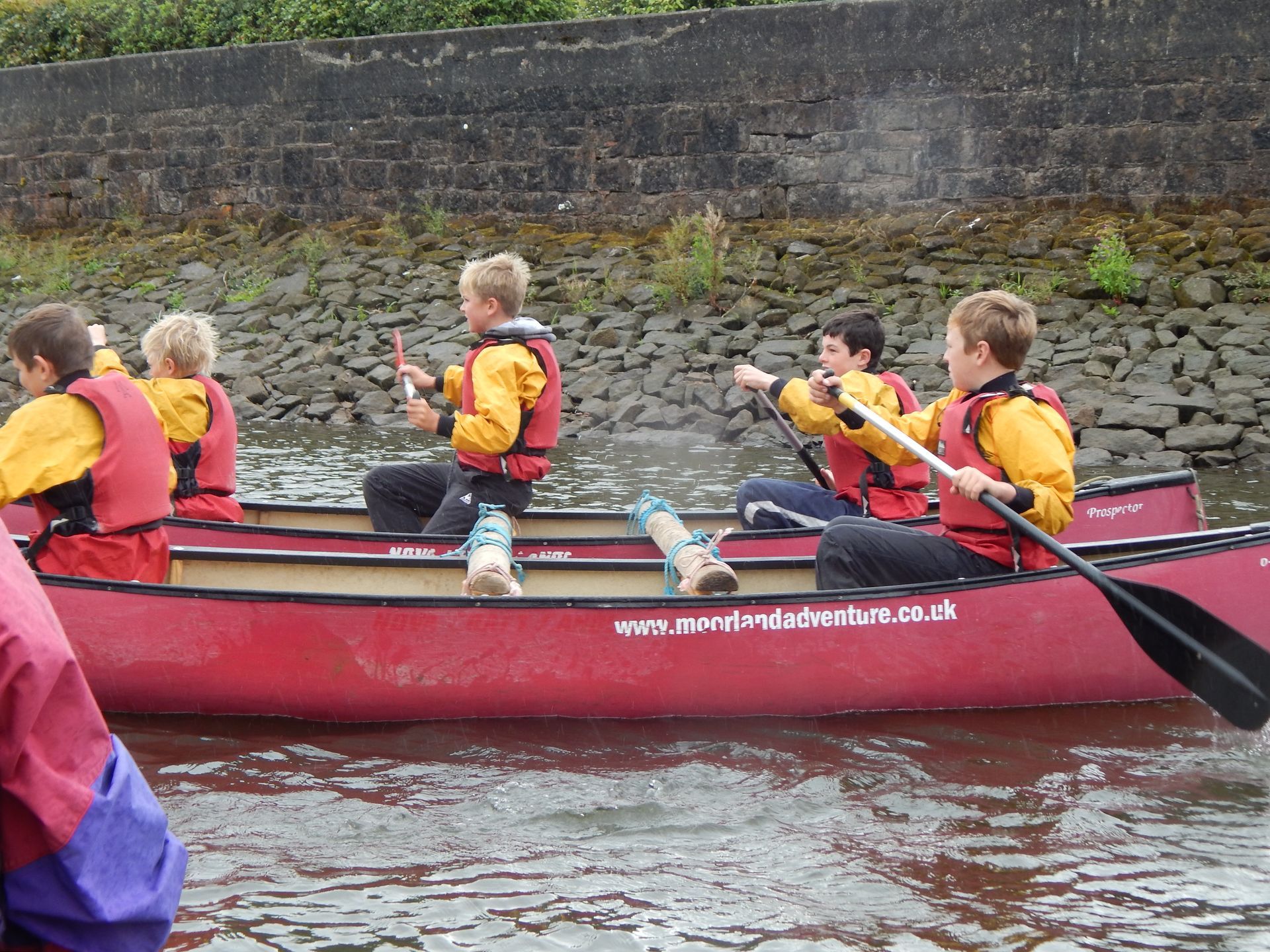 A group of children are paddling a red canoe on a river