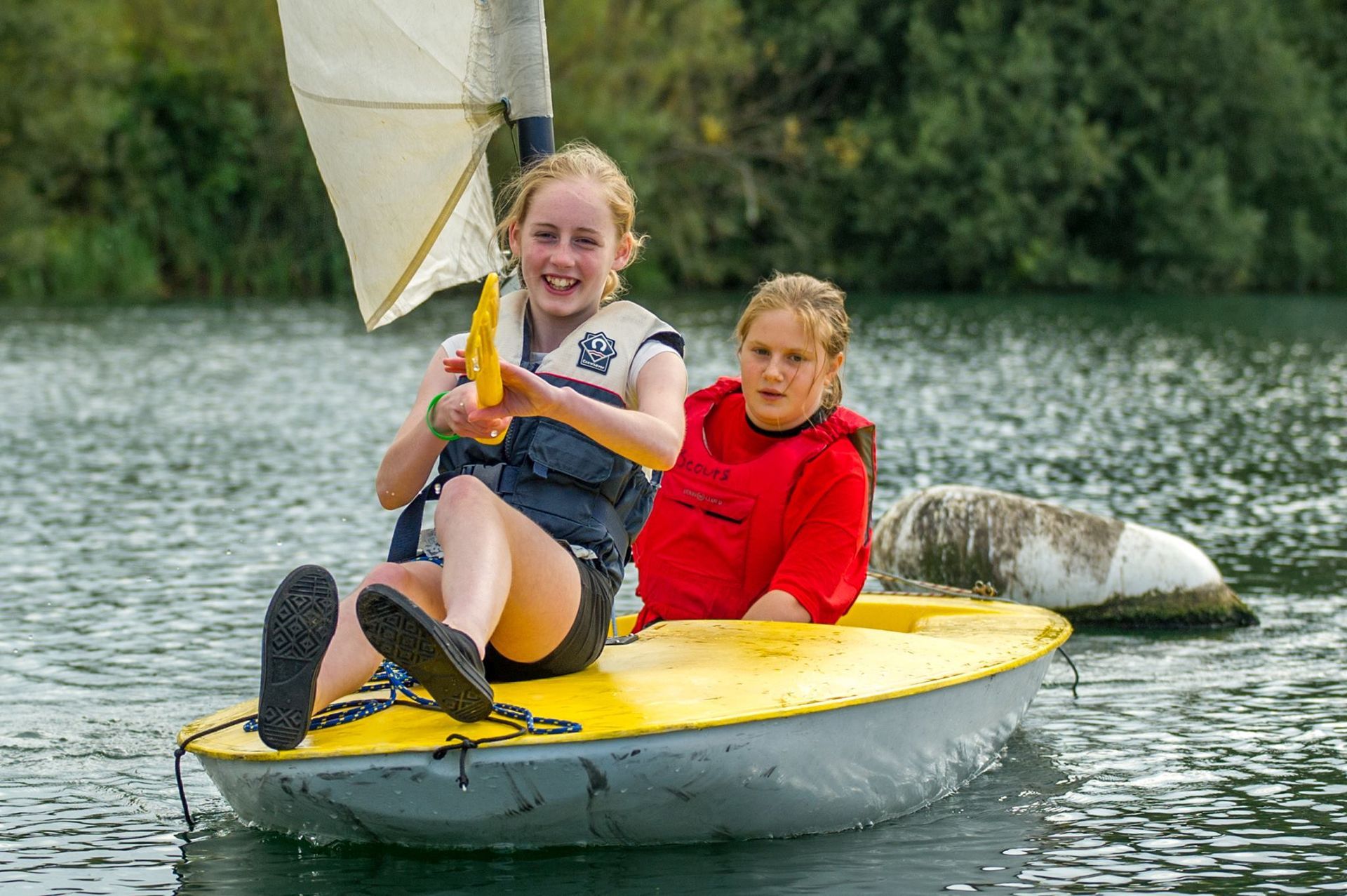 Two young girls are sailing a small boat on a lake.
