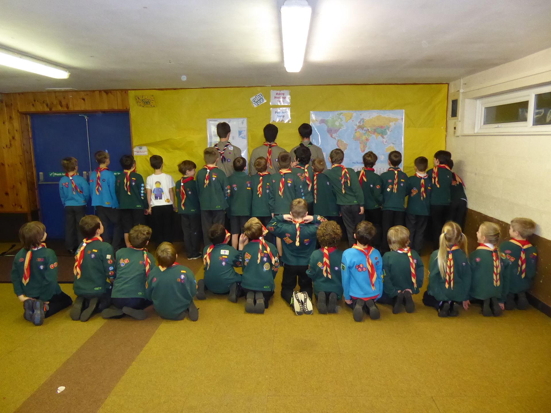 A group of scouts are kneeling down in front of a map of the world