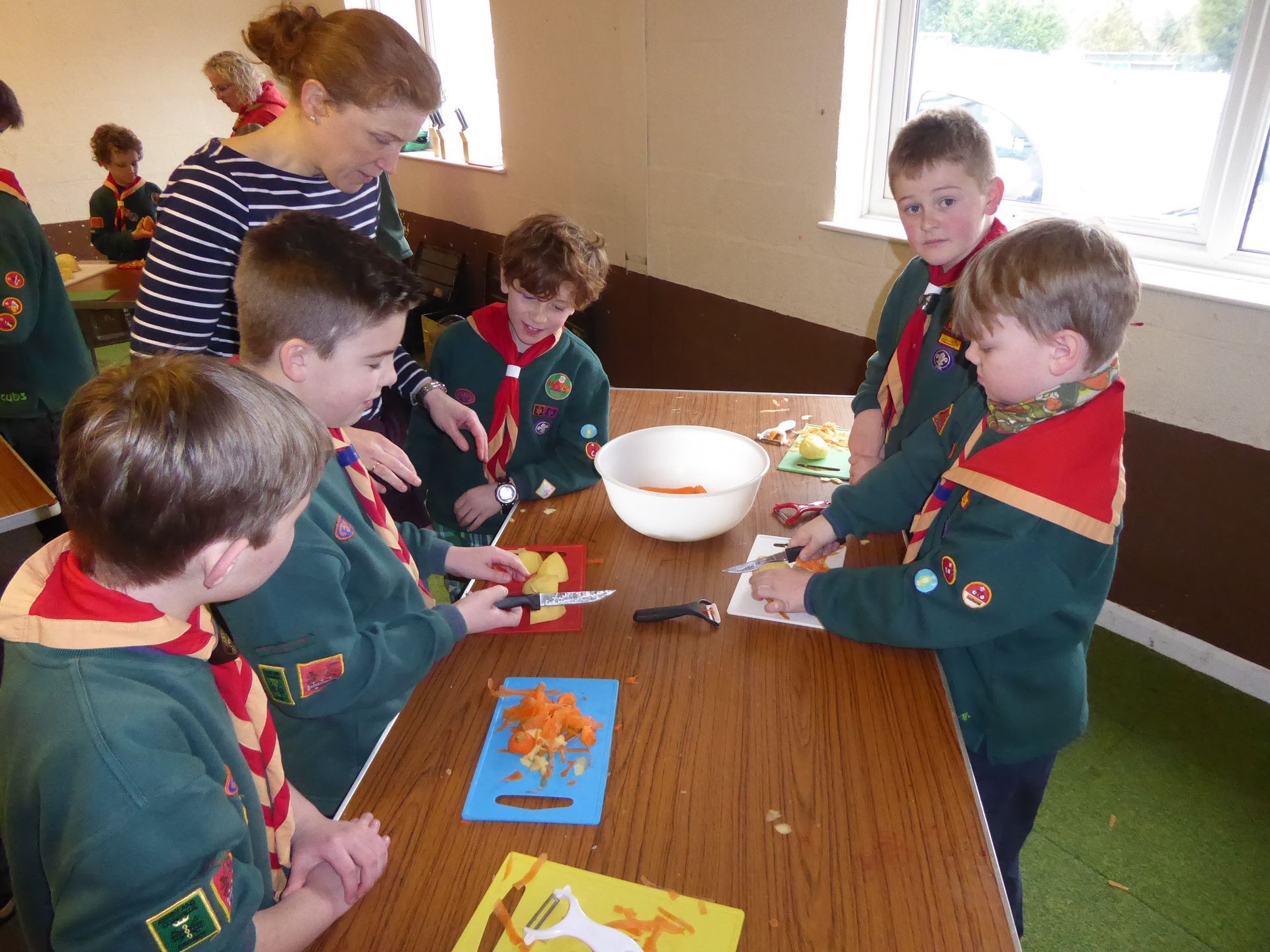 A group of boy scouts are sitting around a table cutting vegetables