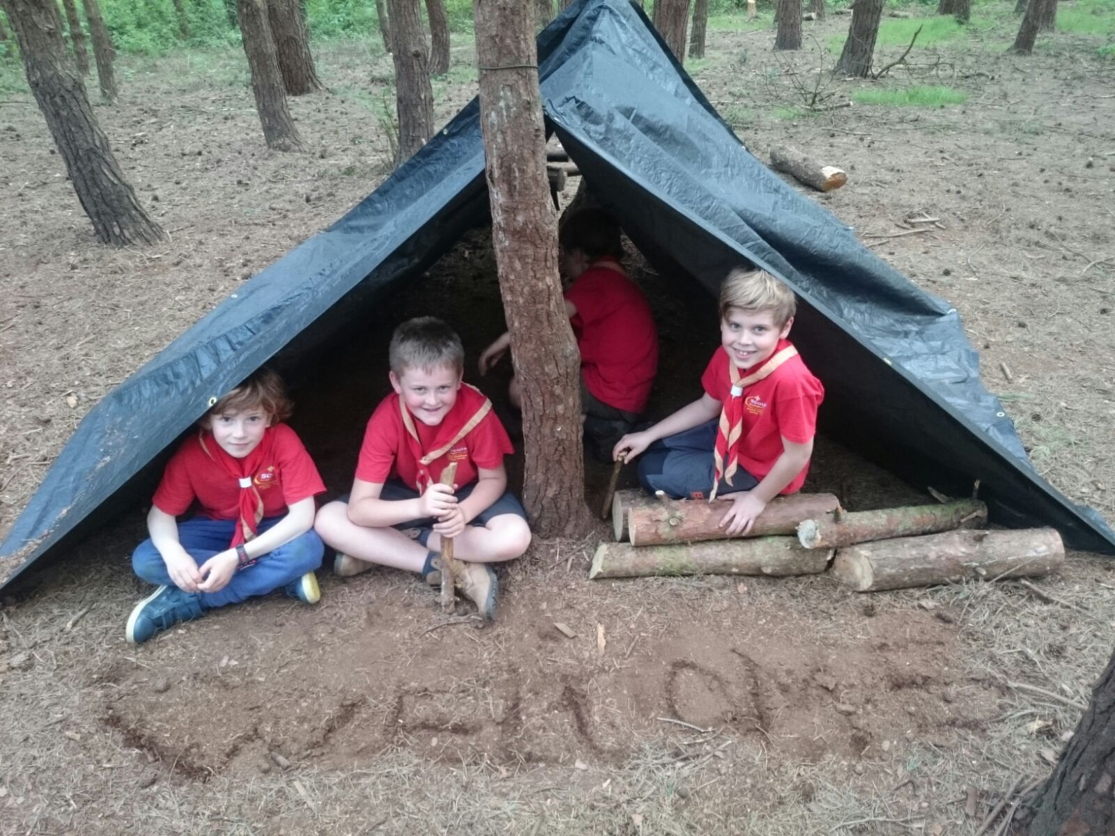 A group of young boys are sitting under a tent with the word welcome written in the dirt