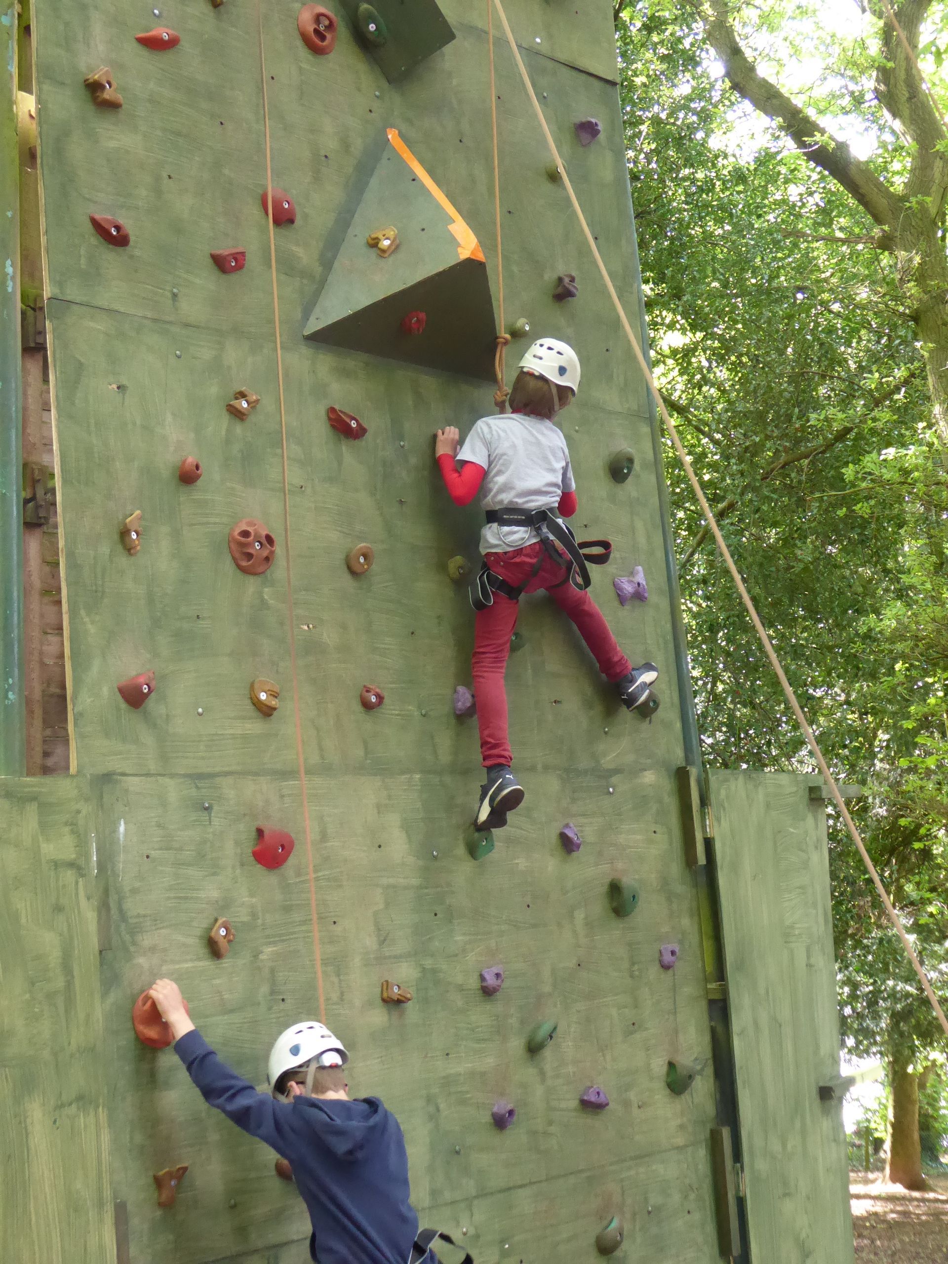Two children are climbing a climbing wall in the woods