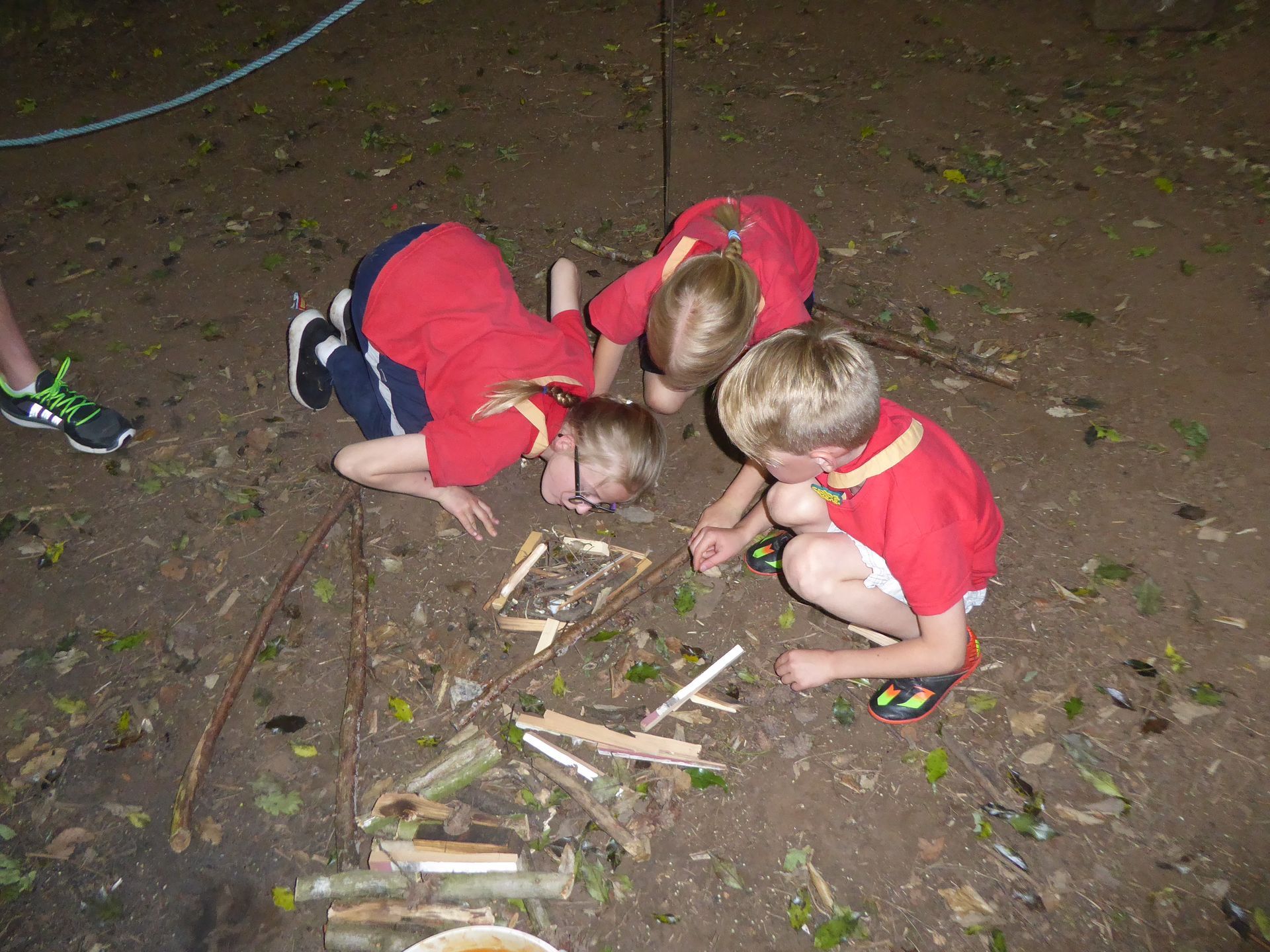 Three young boys in red shirts are playing with wood in the dirt