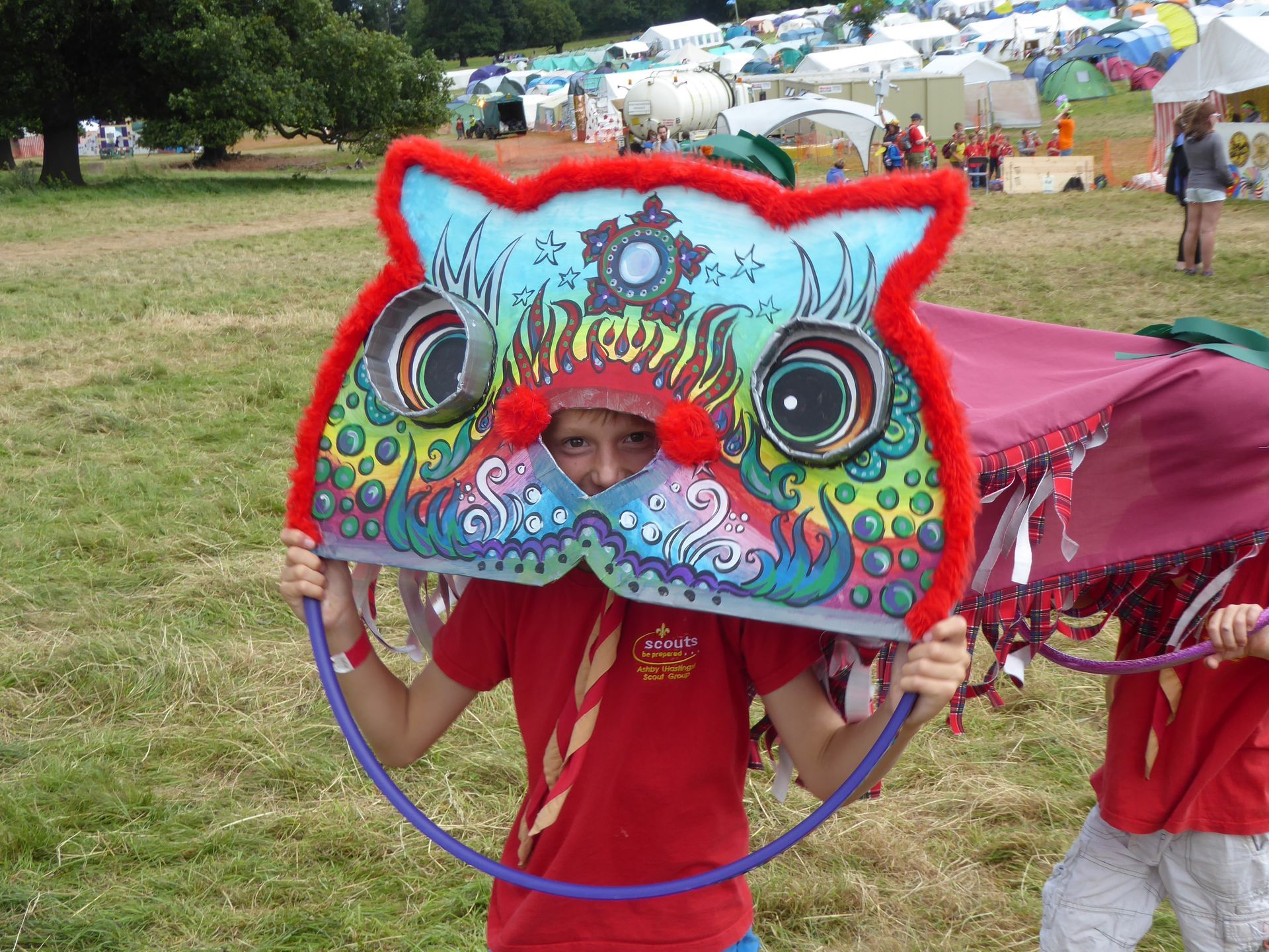 A boy in a red shirt is holding an owl mask over his head