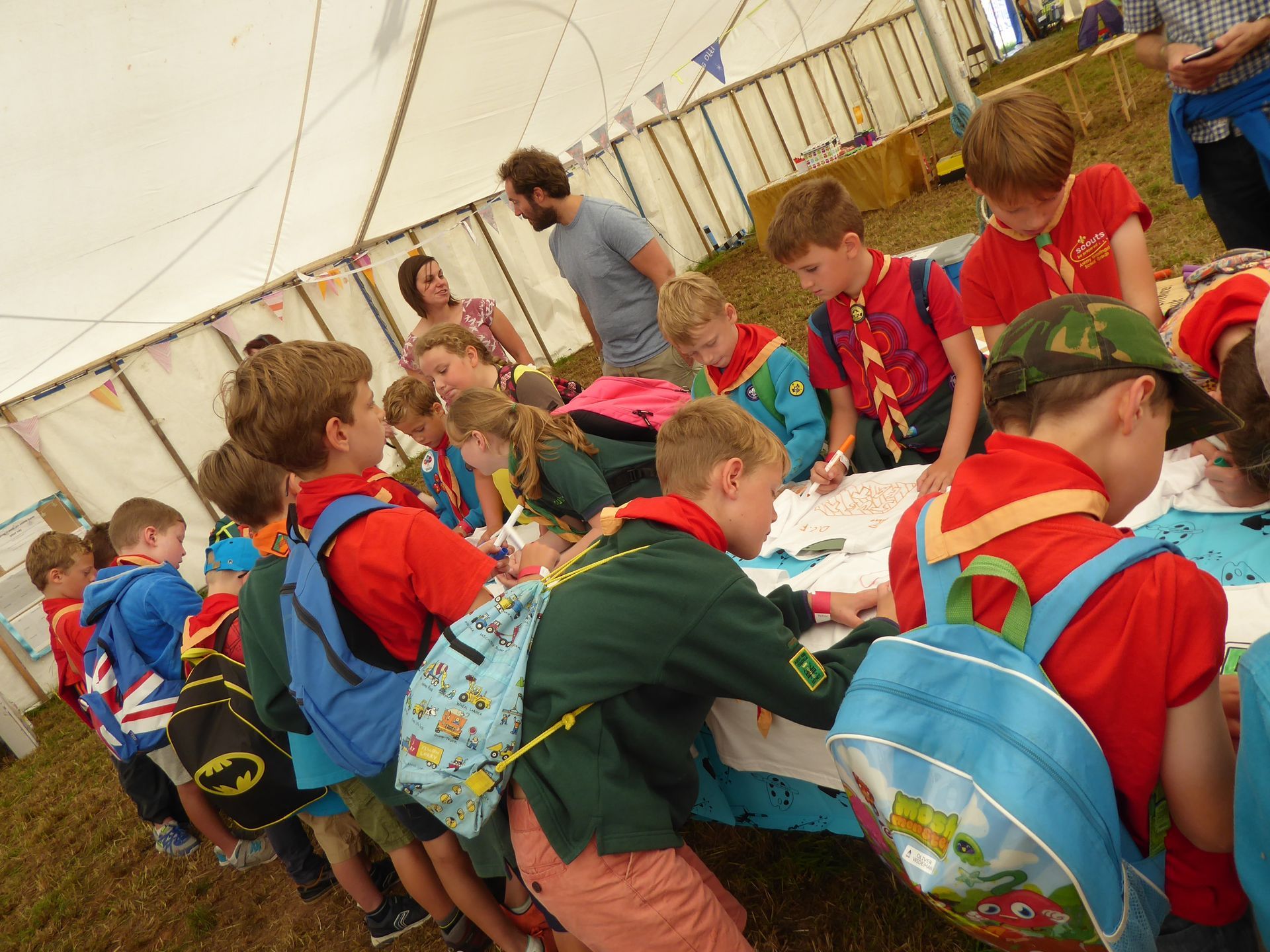 A group of children with backpacks are standing around a table