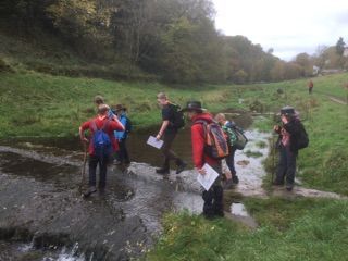 A group of people are standing next to a stream in a field.