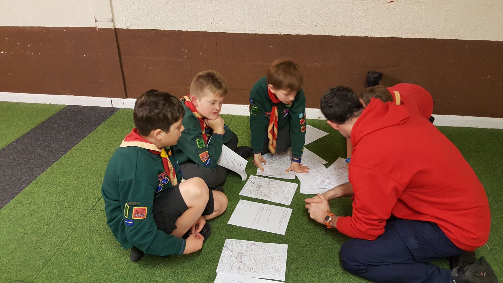 A group of young boys are sitting on the floor looking at papers.