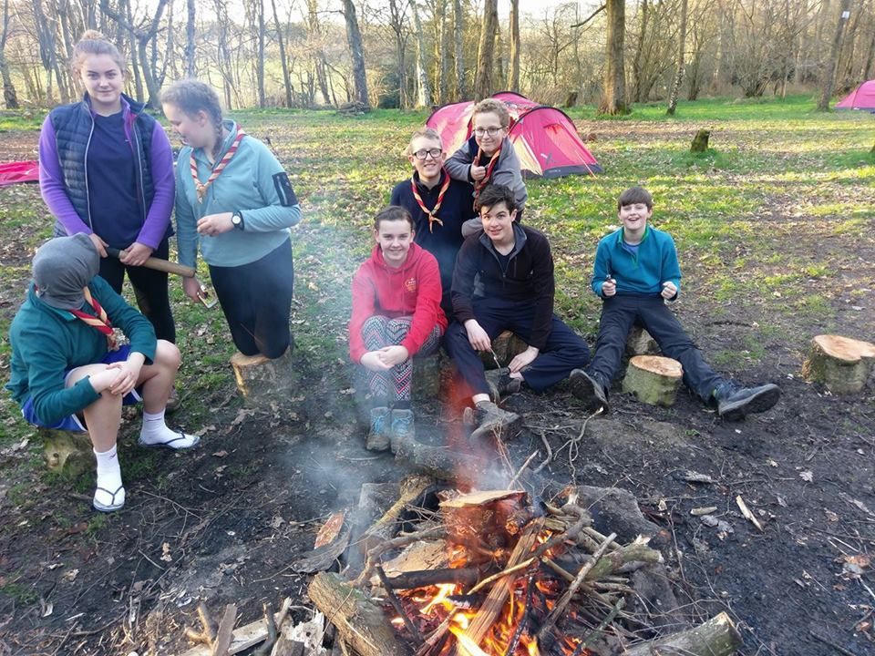A group of people are sitting around a campfire in the woods.