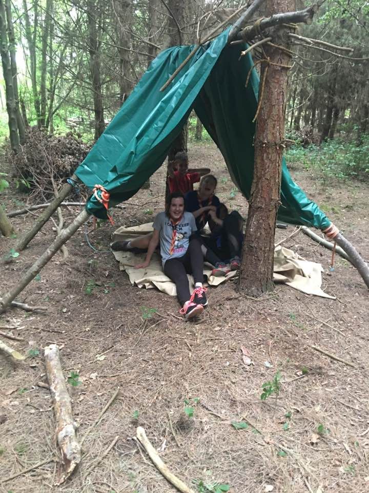 A group of people are sitting under a tarp in the woods.