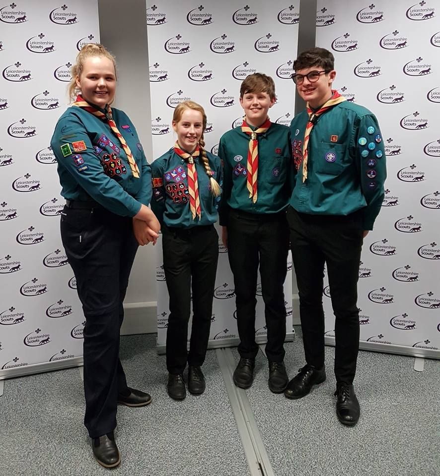 A group of young people are standing next to each other in front of a white wall.