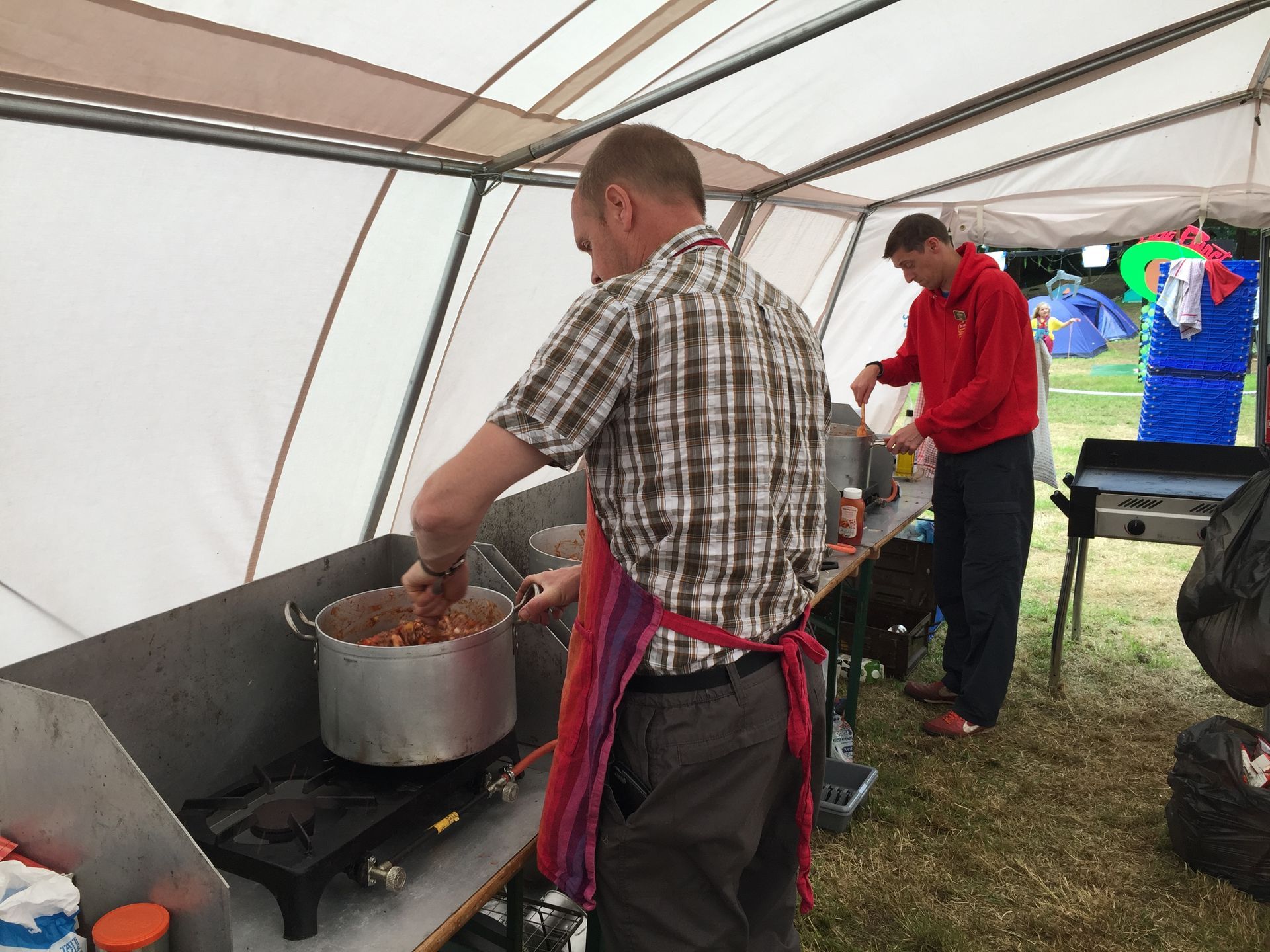 A man in a plaid shirt is preparing food in a tent