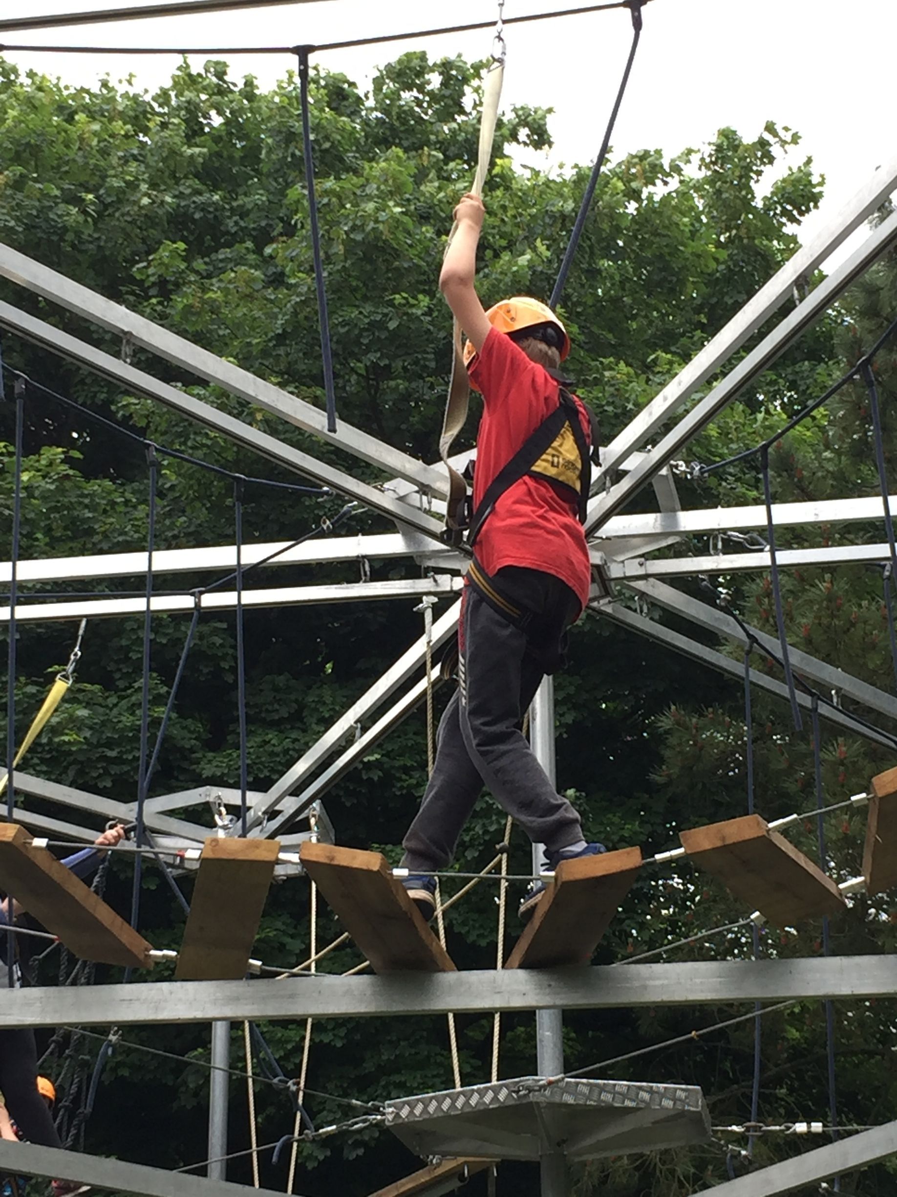 A man in a red shirt is walking on a ropes course.