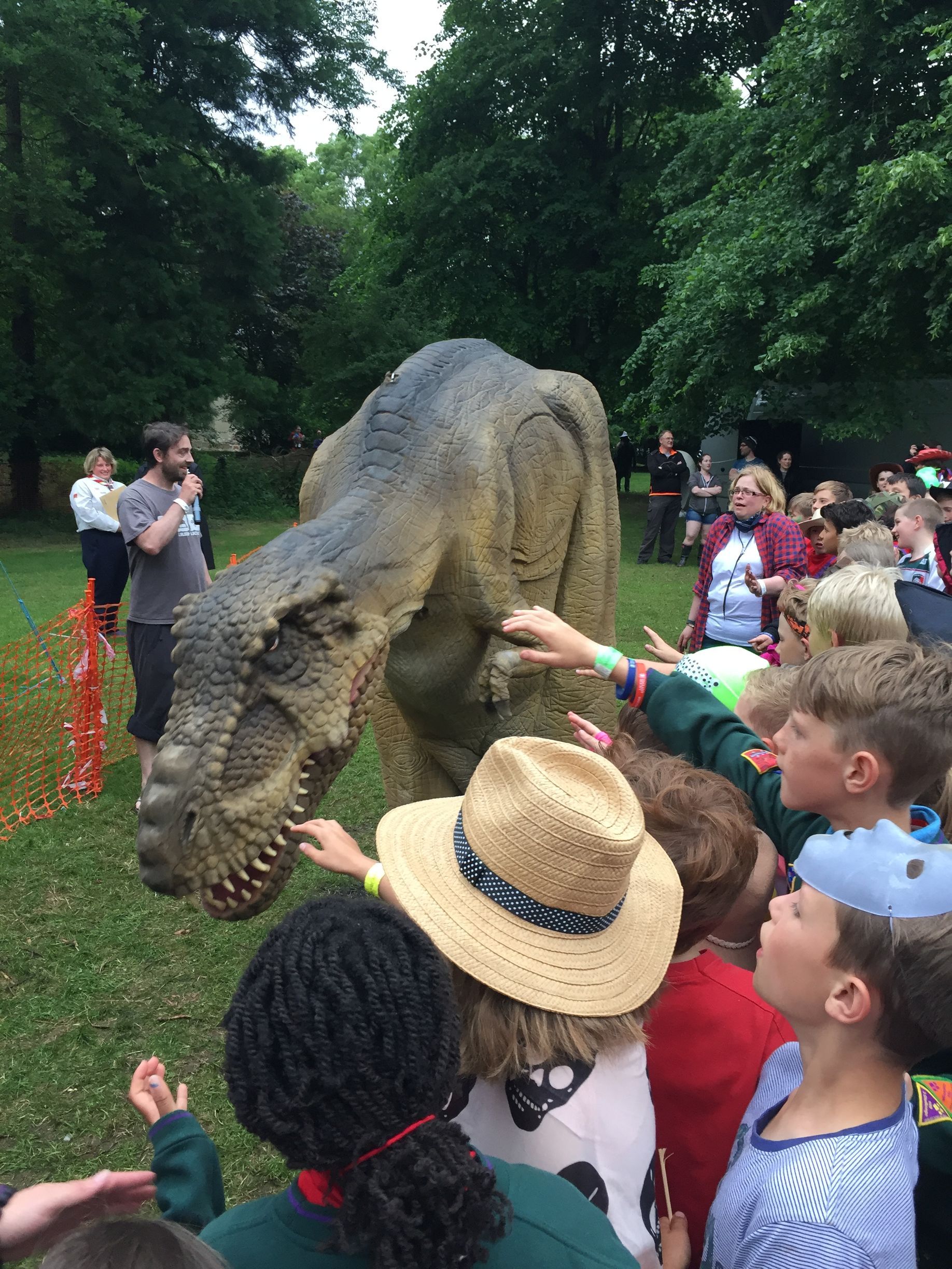 A group of children are touching a dinosaur statue in a park.