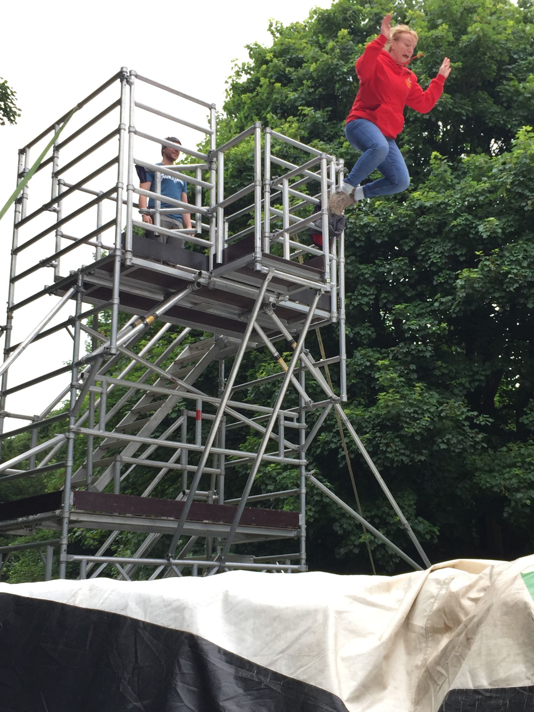 A woman in a red jacket is jumping off a scaffolding