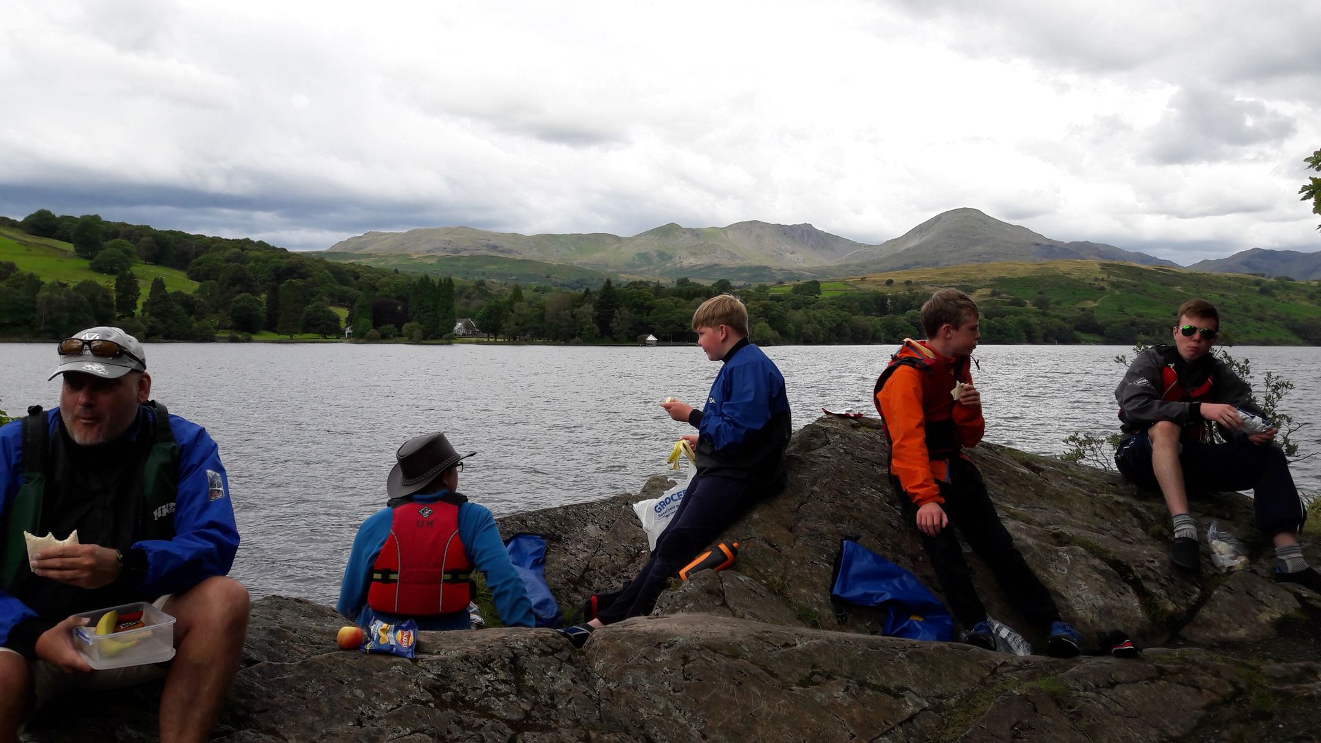 A group of people are sitting on a rock near a lake.