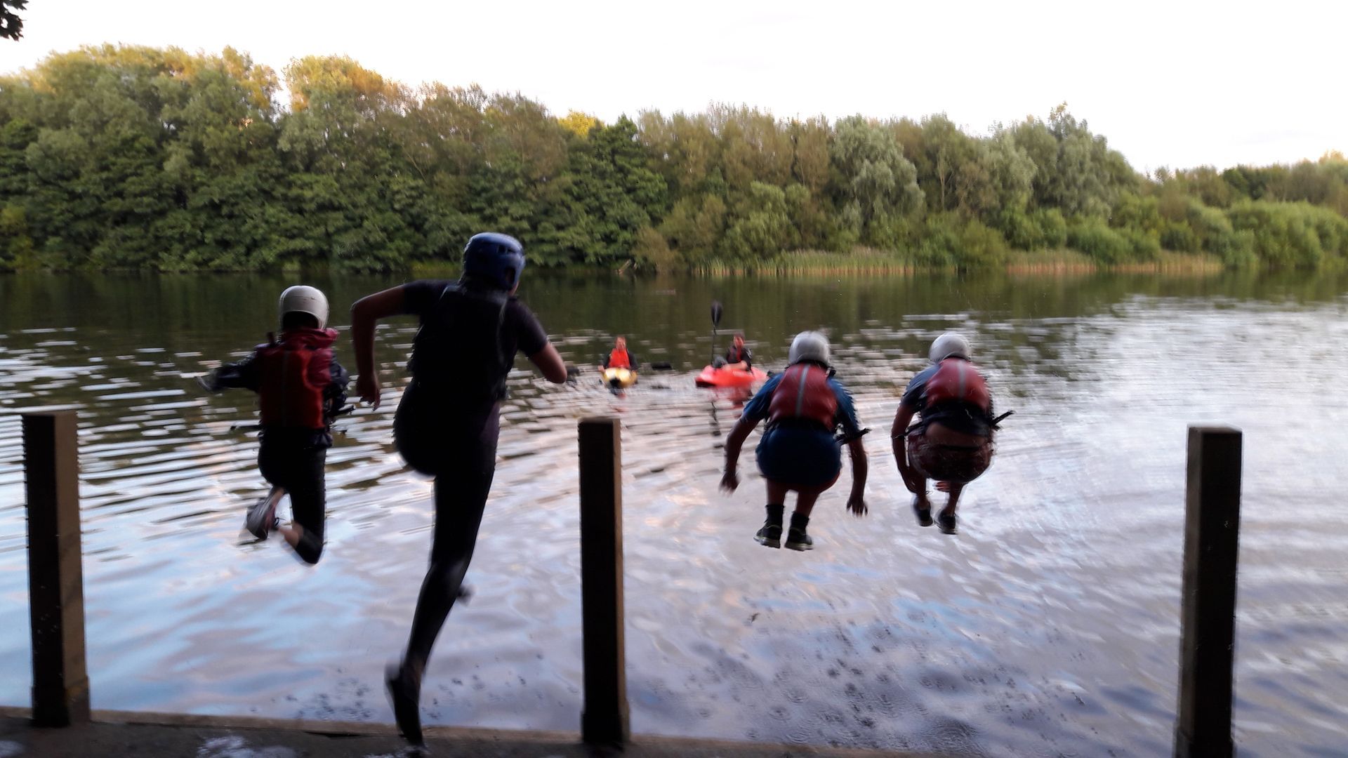 A group of people are jumping into a lake.