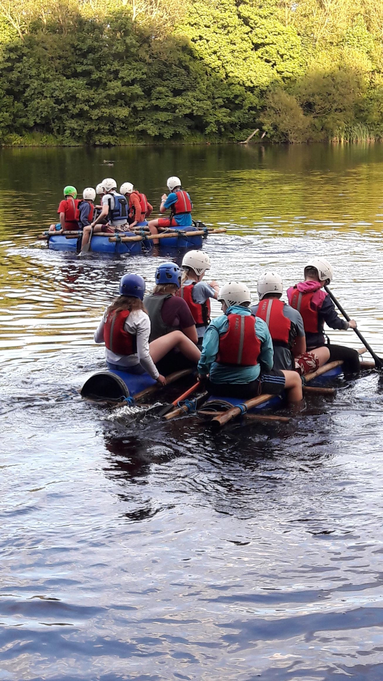 A group of people are rowing rafts down a river.