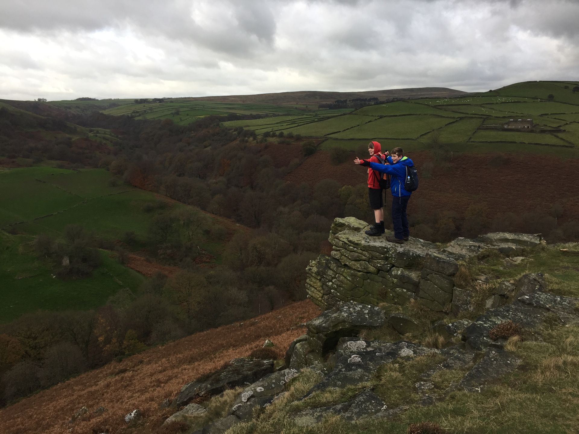 Two people are standing on top of a rocky cliff overlooking a valley.