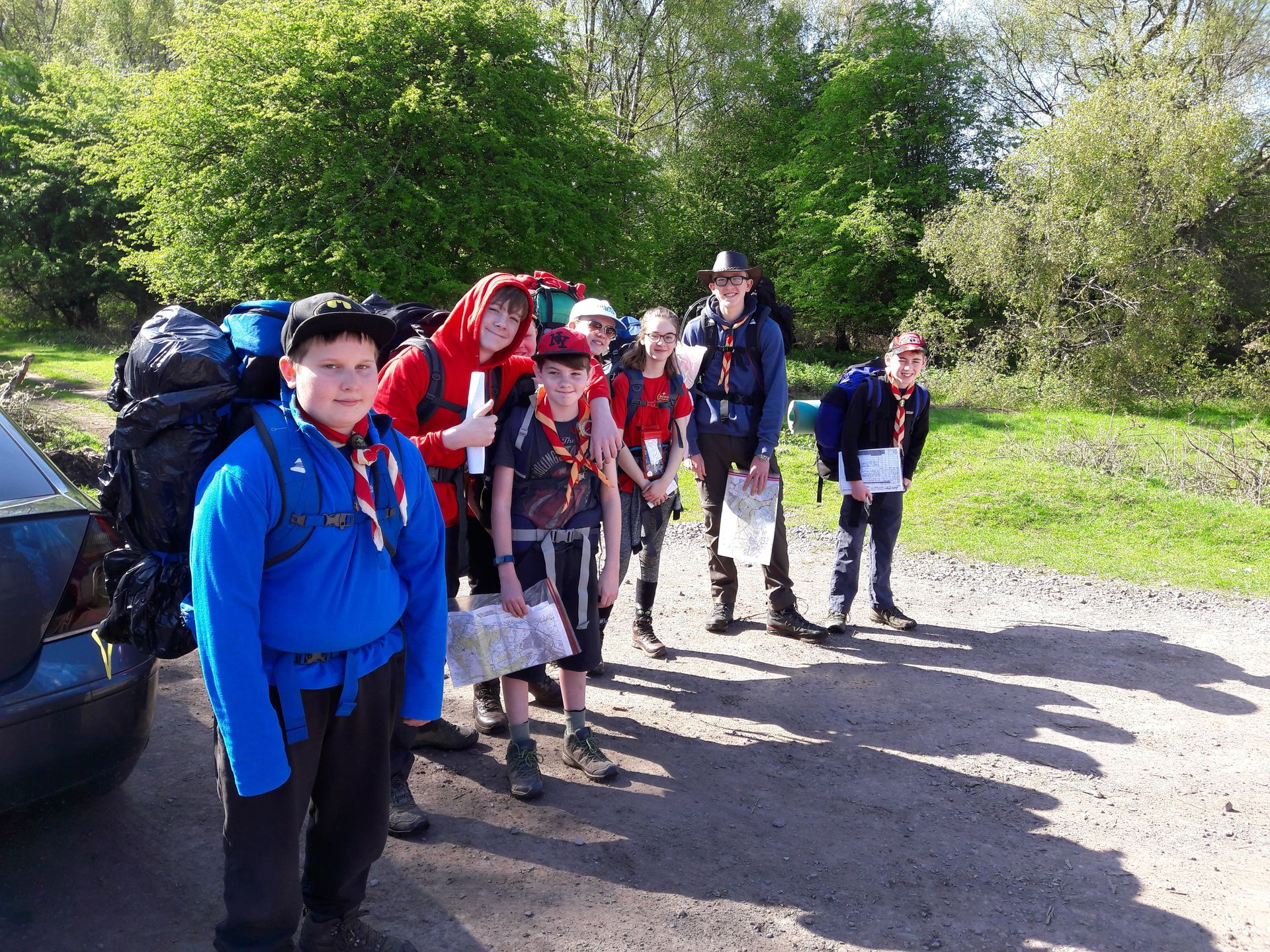 A group of young people with backpacks are standing in front of a car.