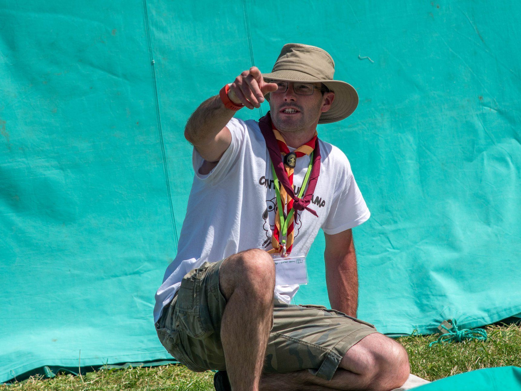 A man wearing a hat is kneeling down and pointing at something.