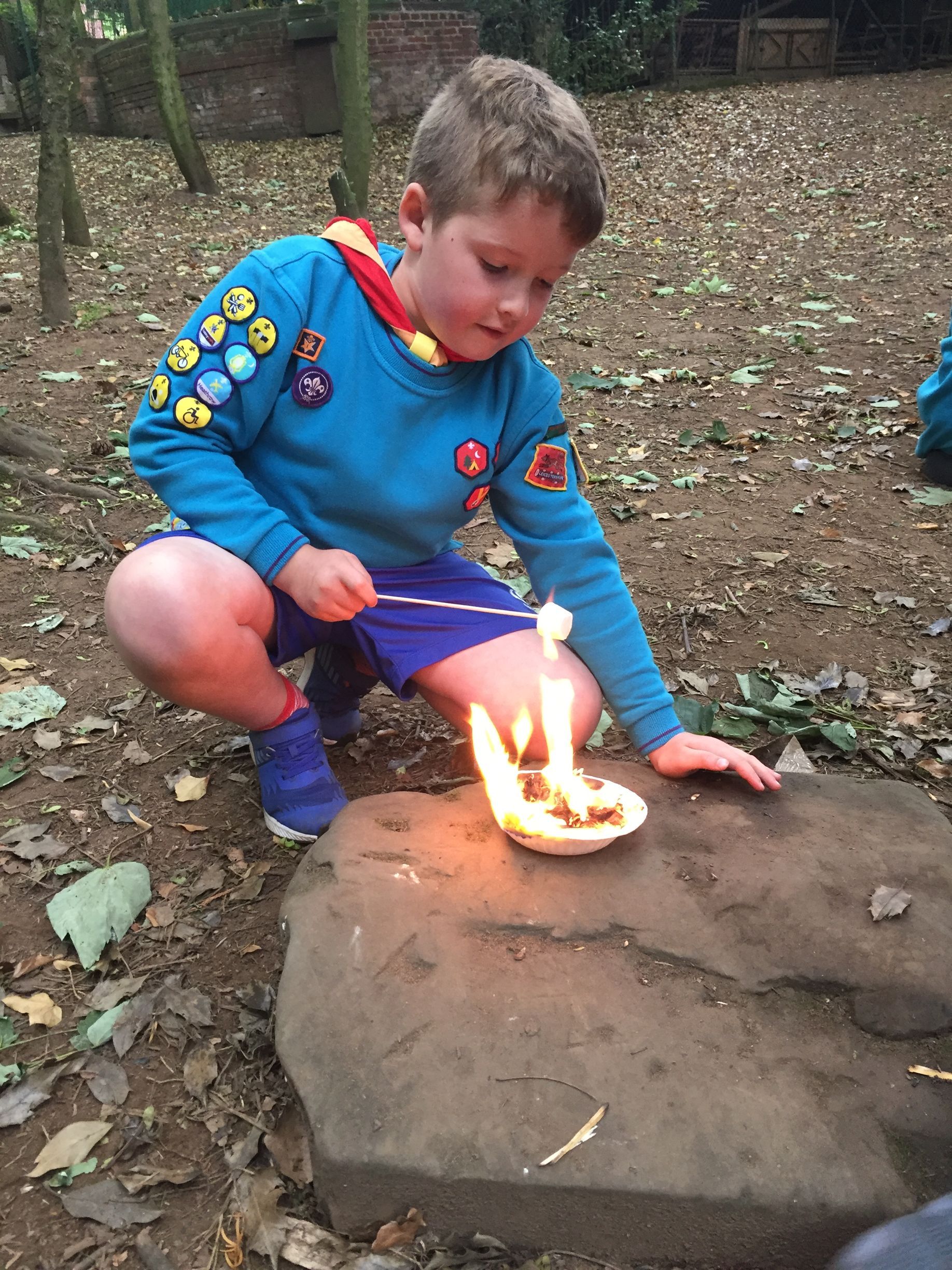 A young boy is kneeling on a rock with a candle in a bowl.