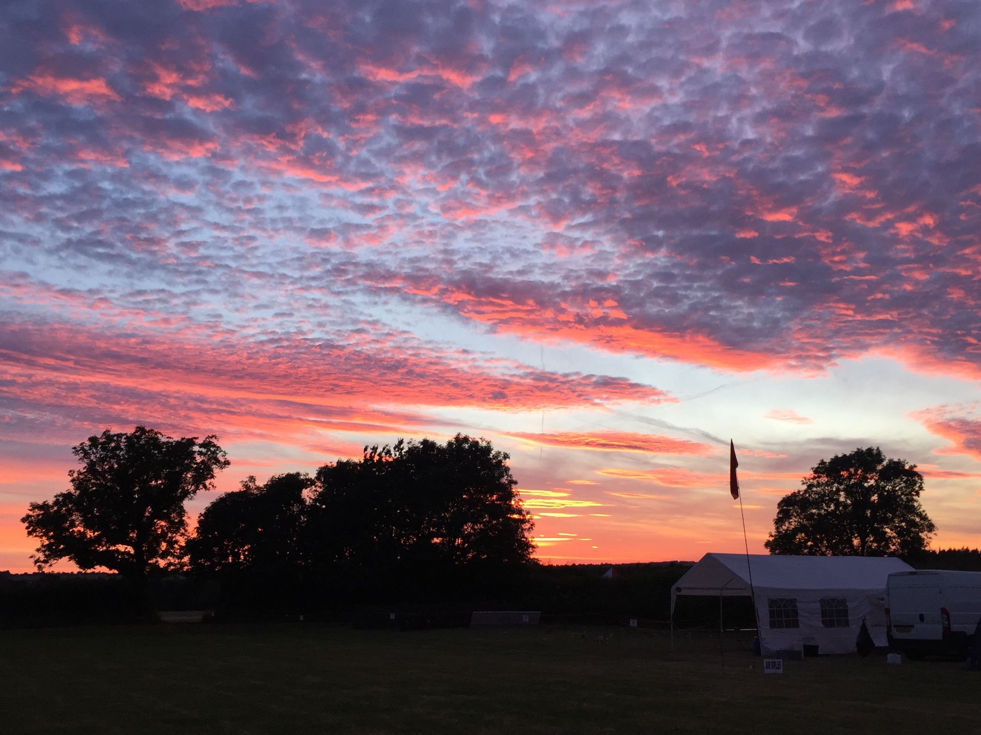 A sunset with a tent in the foreground and trees in the background