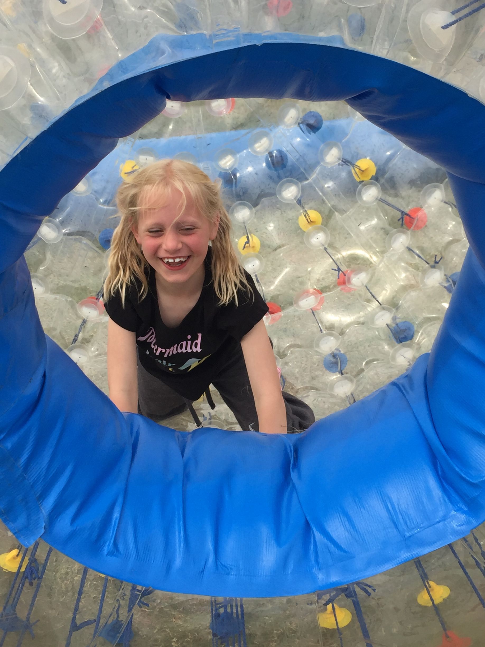 A little girl in a black shirt is playing in a bubble ball.