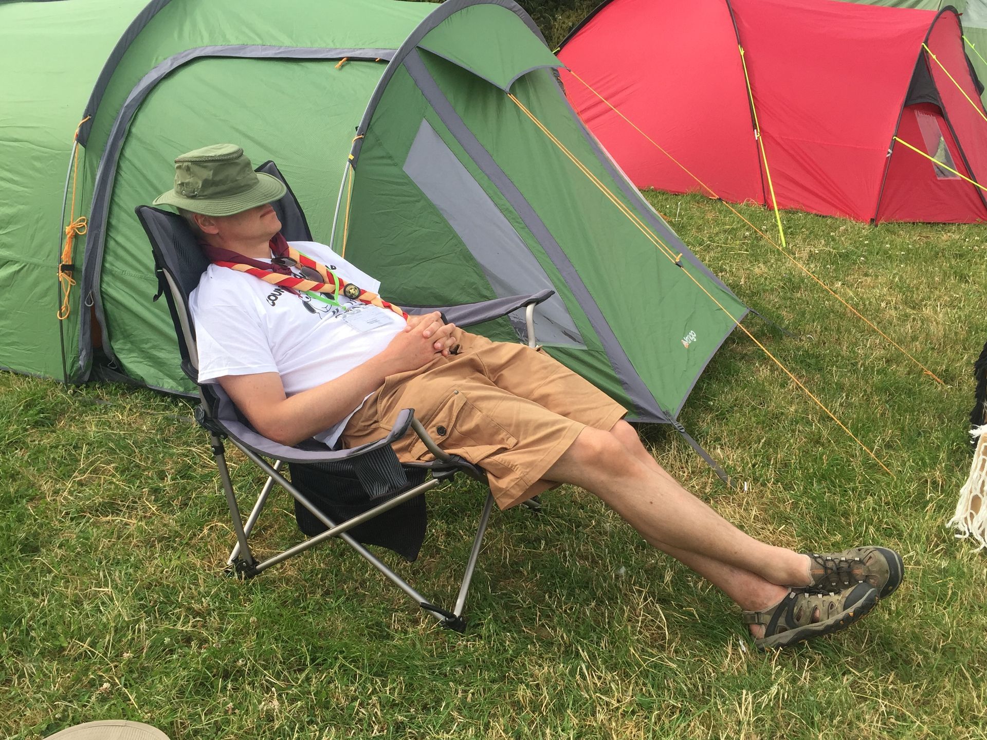 A man is laying in a chair in front of tents
